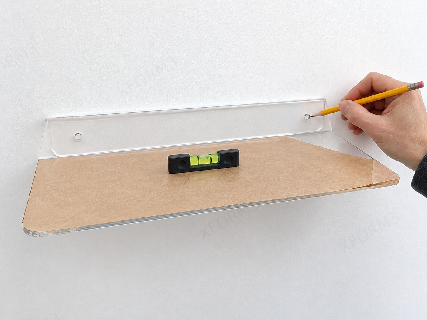 Complete clear acrylic shelf held level at the wall while a pencil marks a mounting hole